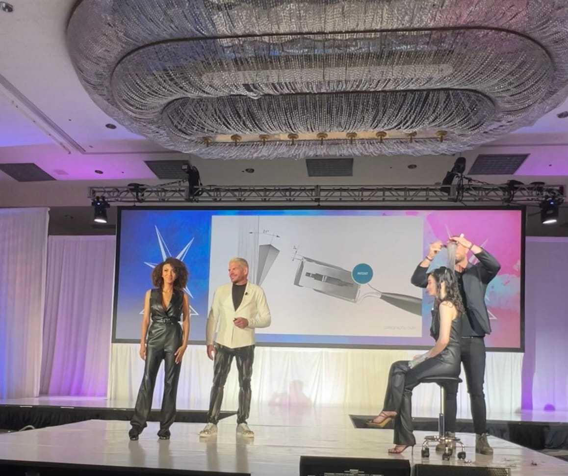 Four people on stage, presenting a design with a large chandelier overhead and a screen behind them.