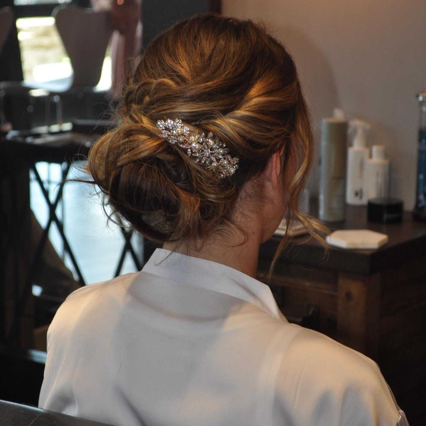 Woman with elegant updo hairstyle and decorative hairpiece sitting in a salon chair.