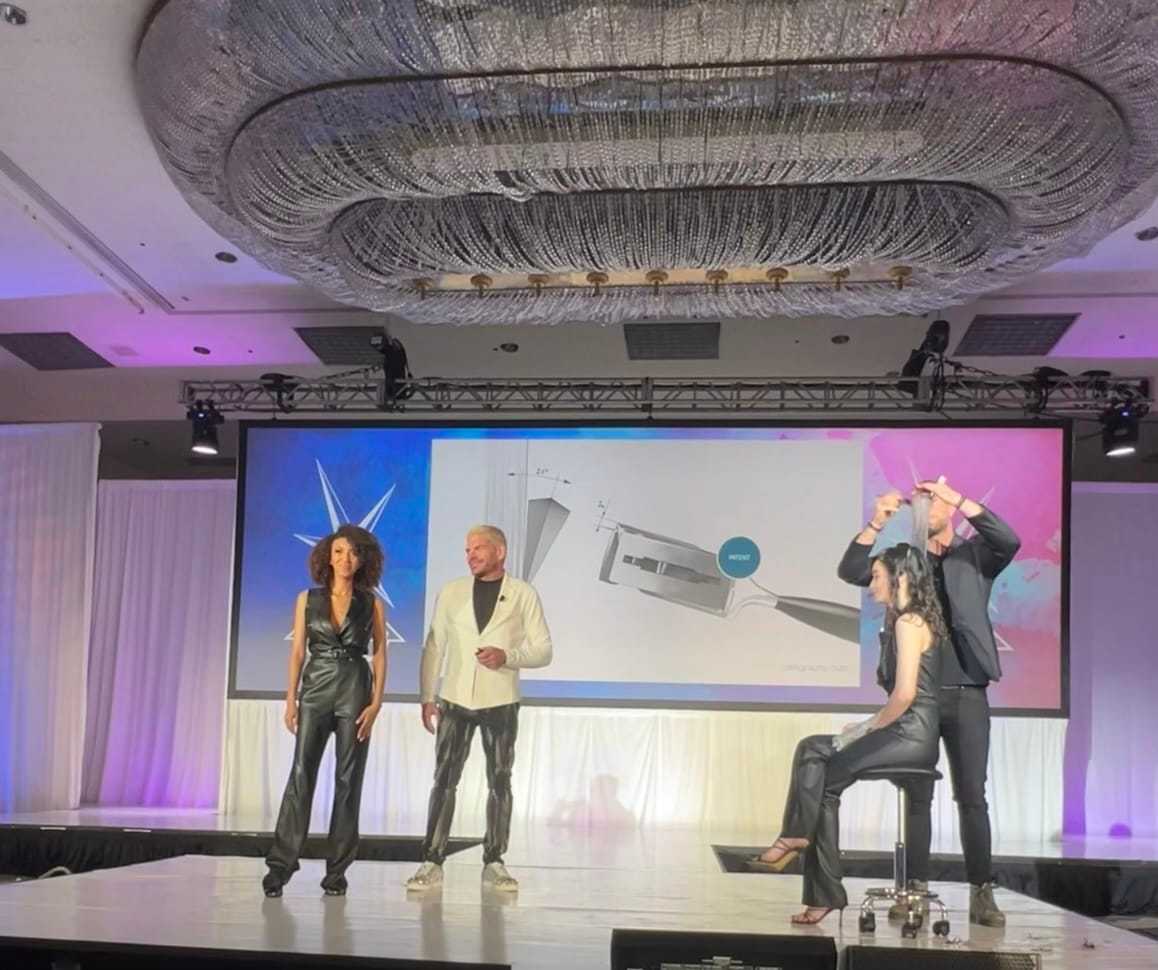 Four people on stage, presenting a design with a large chandelier overhead and a screen behind them.