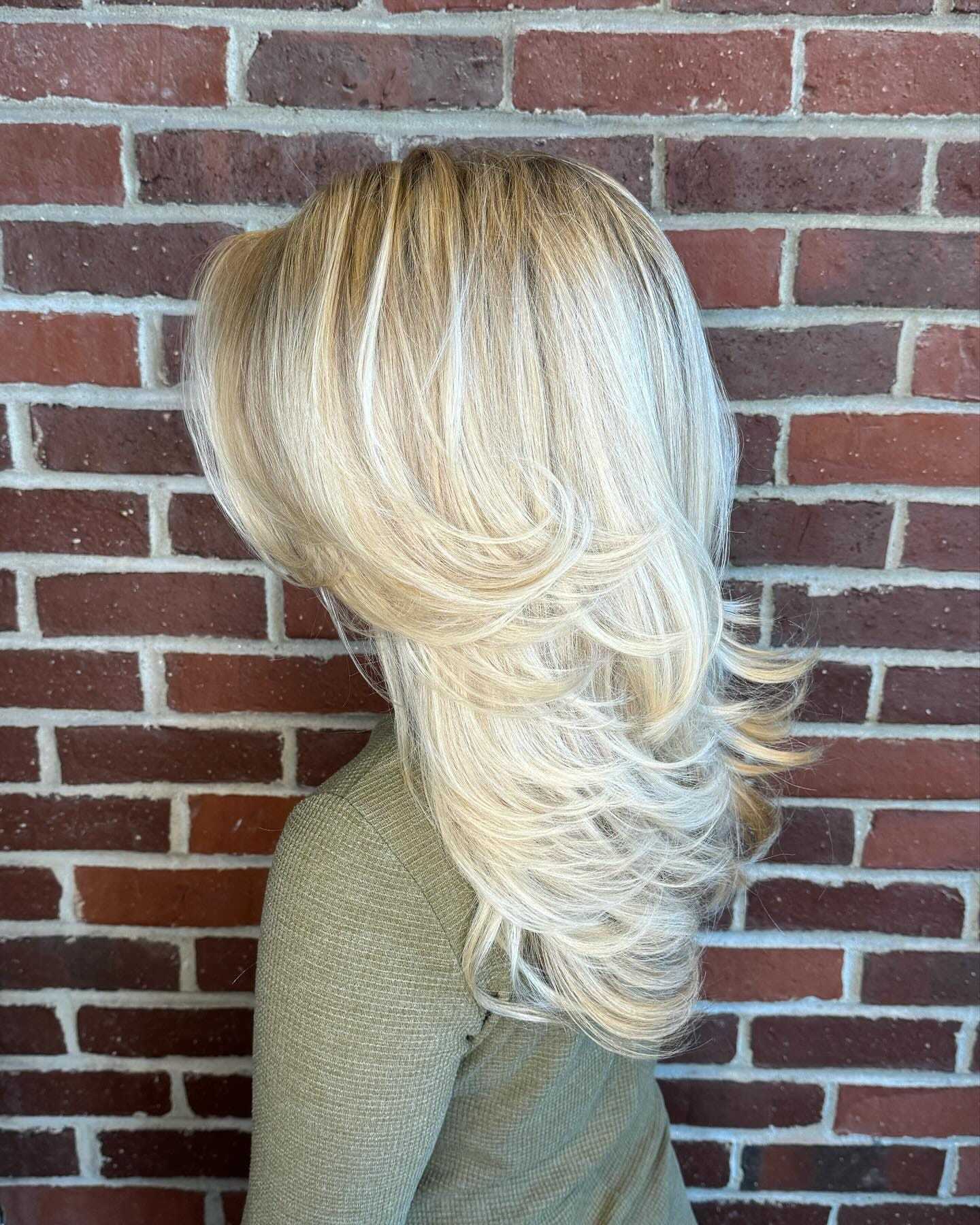 Woman with layered blond hair against a brick wall.